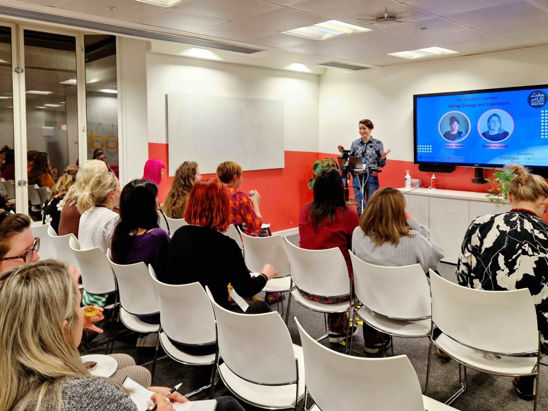Person giving talk at the front of room setup with chairs in a lecture-style format.