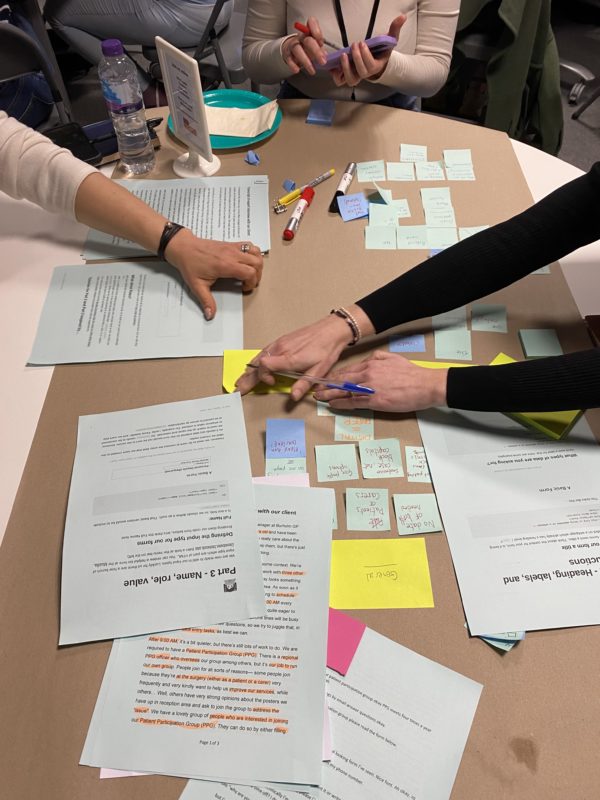 Three people's hands working with sticky notes and papers on a table at a workshop.