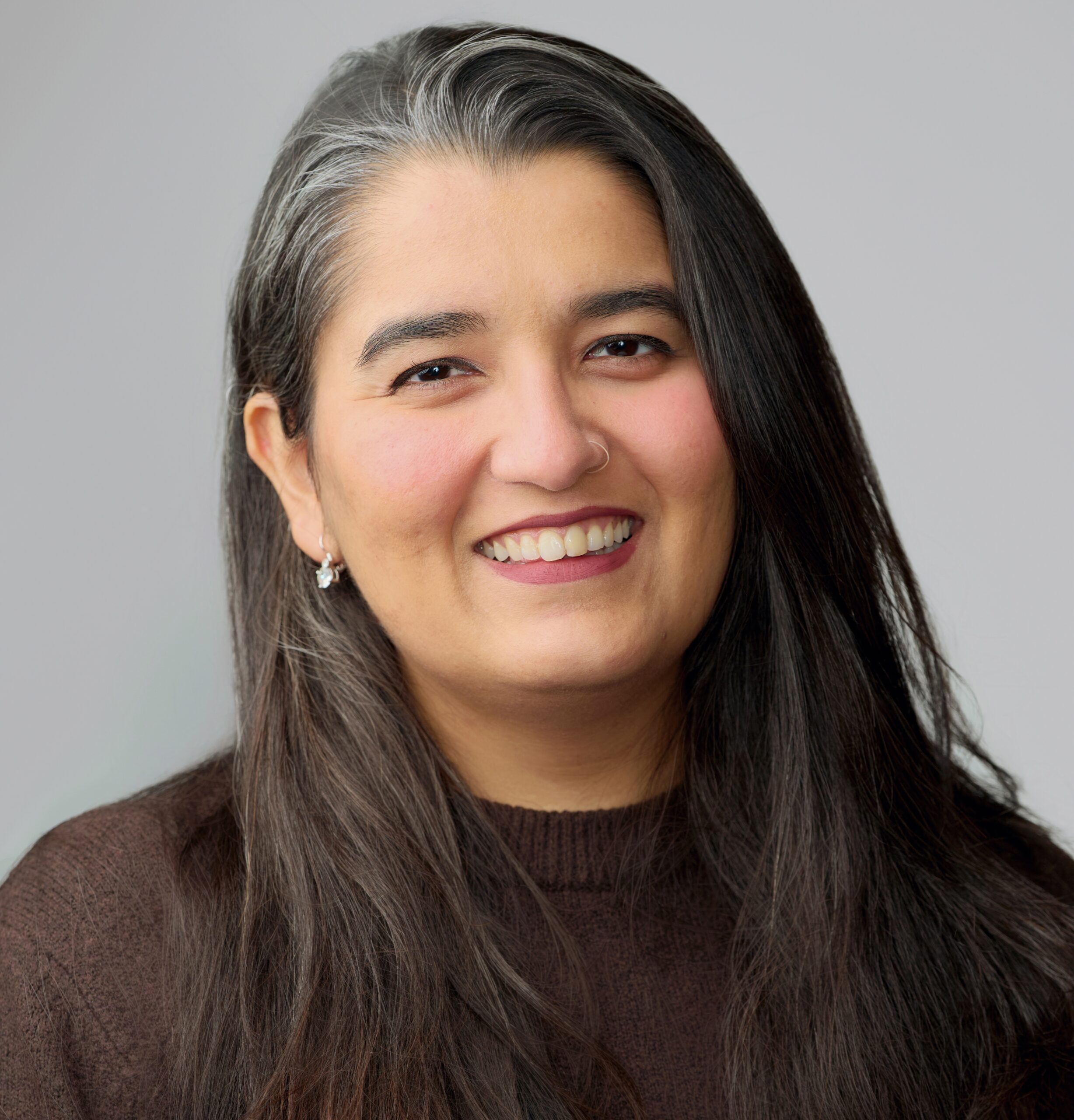 Deeksha Bhushan in a brown jumper in front of a neutral background